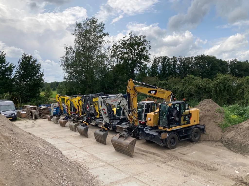 Rij graafmachines van Van den Hurk op een zandplateau, voorop een gele wielgraafmachine